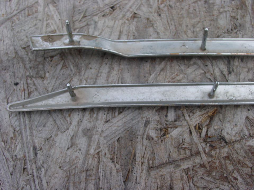 Two chrome trim pieces with mounting studs on a wooden background.