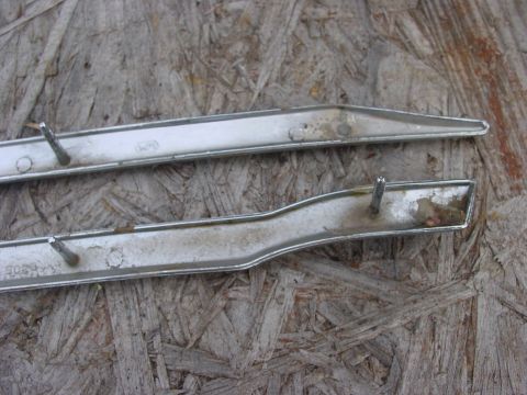 1973 Ford Ranchero - Two pieces of chrome trim with mounting studs are shown against a textured wooden background. The trim pieces appear to be from a vehicle,…