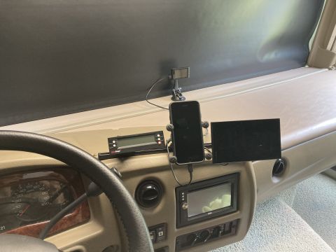 2015 Ford F-550 - The interior dashboard of a motorhome shows a steering wheel, gauges, a smartphone mounted on a dash mount, a small screen, and a digital d…