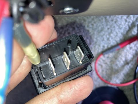 2015 Ford F-550 - A hand holds a black three-terminal rocker switch with silver metal connectors. Wires with blue and yellow insulation are connected to the…
