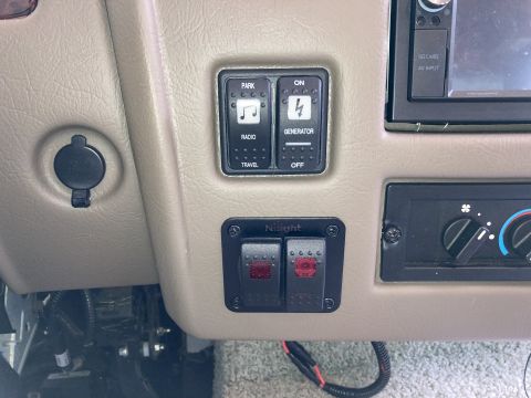2015 Ford F-550 - A close-up view of the dashboard of an RV, showing a 12V power outlet, a bank of control switches for park, radio, and generator functions,…