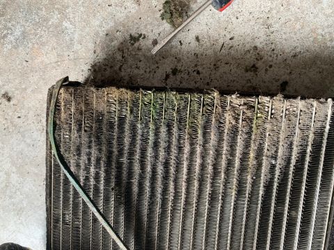 2008 Ford Focus - A close-up view of a very dirty and clogged car radiator or condenser. The fins are packed with debris, including dirt, grass, and what app…