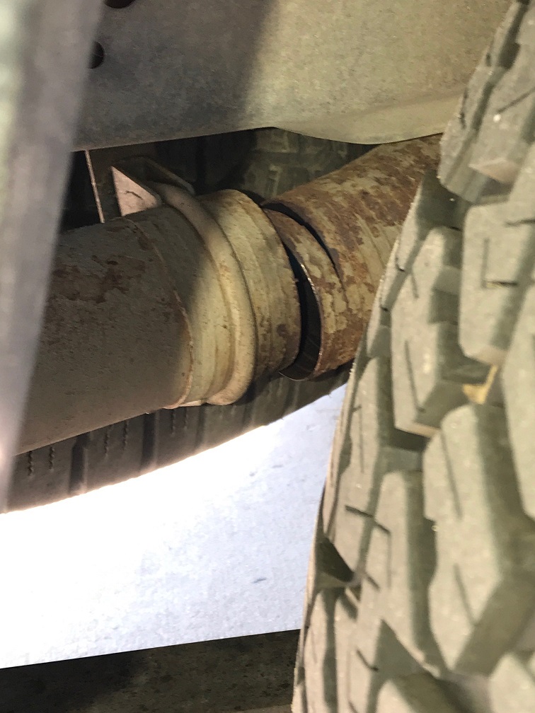 Close-up of a rusty driveshaft with a gap, near a vehicle tire.