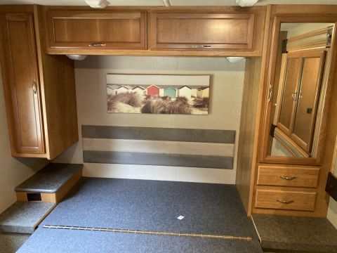 2015 Ford F-550 - The interior of a recreational vehicle features a bed, wooden cabinets, and a painting of beach houses.