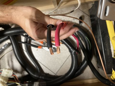 2015 Ford F-550 - A person's hands hold two stripped electrical wires, one black and one red, with a bundle of black corrugated tubing and other wiring visib…