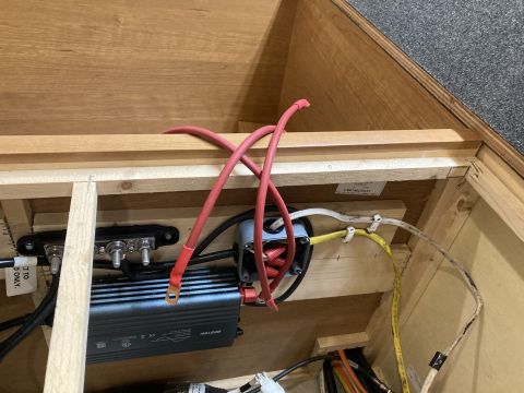 2015 Ford F-550 - A close-up view of electrical wiring and an inverter installed inside a wooden compartment, likely within a vehicle or RV. Thick red cables…