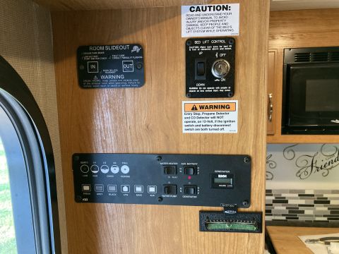 2015 Ford F-550 - A panel of RV controls is mounted on a wood-paneled wall, featuring slideout controls, a bed lift control, and tank level indicators.