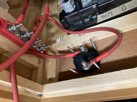 2015 Ford F-550 - A close-up view shows red battery cables connected to a red bus bar and a black terminal block, all mounted within a wooden enclosure.