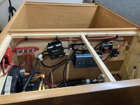2015 Ford F-550 - A close-up view of electrical components installed inside a wooden compartment, including a battery, inverter, and wiring.