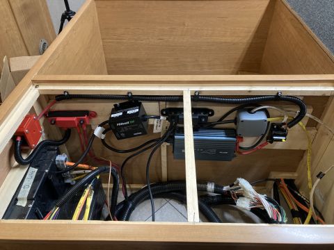 2015 Ford F-550 - The interior of a vehicle storage compartment shows a complex electrical system with batteries, an inverter, fuses, and wiring harnesses.