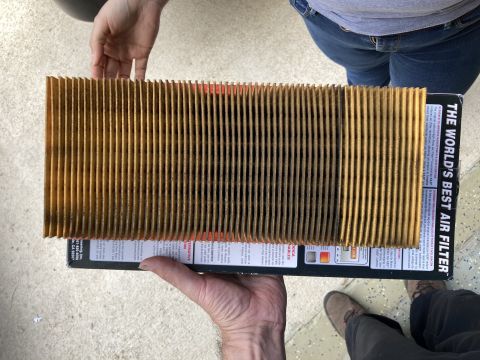 2015 Ford F-550 - A dirty, pleated air filter is held by two people over its black and white packaging. The packaging has text that reads "THE WORLD'S BEST A…