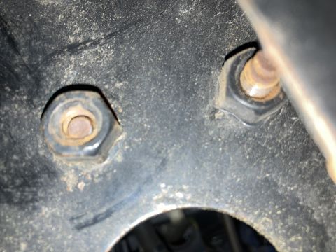 2015 Ford F-550 - Two rusty nuts are visible on a black, dusty surface. The nuts appear to be hexagonal and are threaded onto bolts. A portion of a dark, ang…
