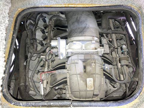 2015 Ford F-550 - Overhead view of a dusty Ford V8 engine with various hoses, wires, and a large intake manifold. The engine appears to be installed in a veh…