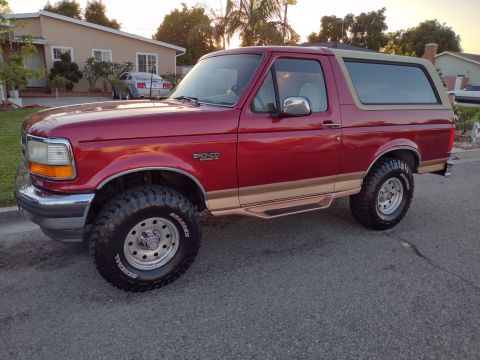 1994 Ford Bronco - This red Ford Bronco with tan trim and aftermarket wheels is parked on a street.