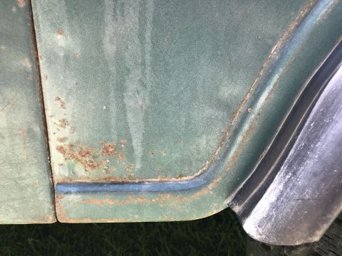 1979 Jeep CJ5 - Rust is visible on the lower edge of a green vehicle's body panel, next to a chrome trim piece.