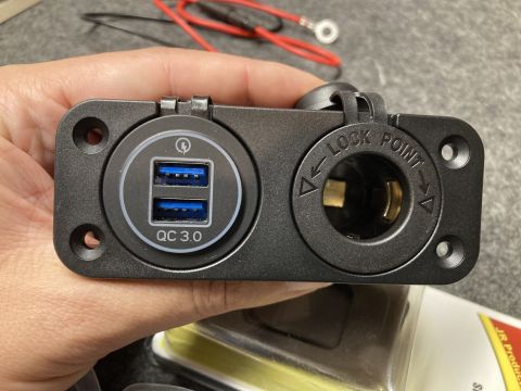 2015 Ford F-550 - A hand holds a black panel with two USB ports and a 12V power socket, along with red wires.