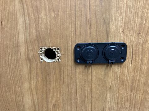 2015 Ford F-550 - A close-up shows a newly installed dual 12V power outlet on a wood-grain surface, with a pre-drilled hole nearby.