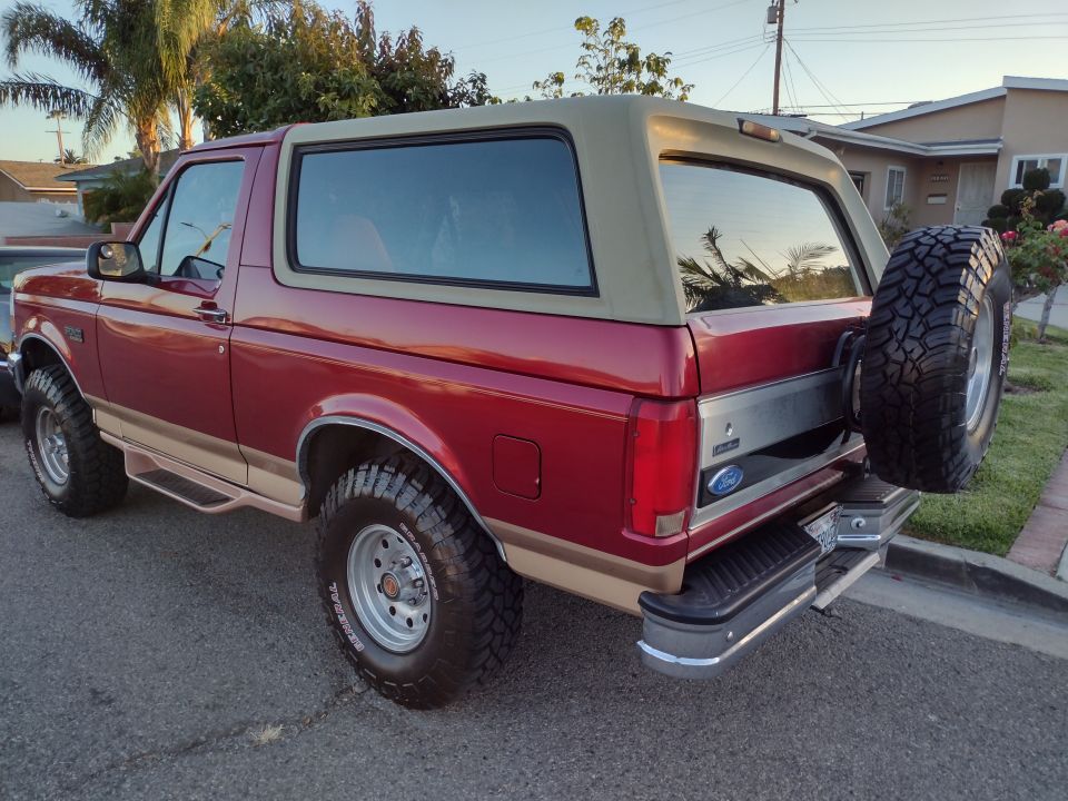 Red and tan Ford Bronco with a spare tire mounted on the rear, viewed from the rear three-quarter angle