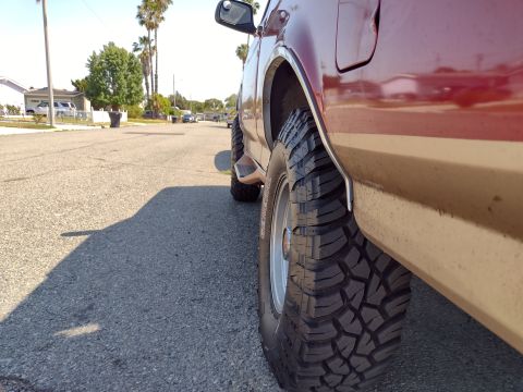 1994 Ford Bronco - Side profile of a red and tan SUV with prominent off-road tires and a running board visible.