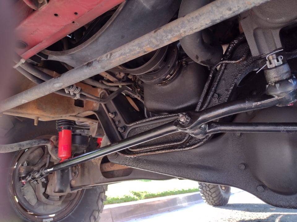 Underside view of a vehicle's suspension and drivetrain components. Red shocks are visible