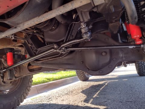 1994 Ford Bronco - The undercarriage of a 1994 Ford Bronco is visible, highlighting the steering components and bright red shock absorbers.