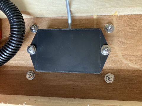 2015 Ford F-550 - A black electronic component, possibly a surge protector, is secured with screws to a wooden surface, with a black conduit nearby.