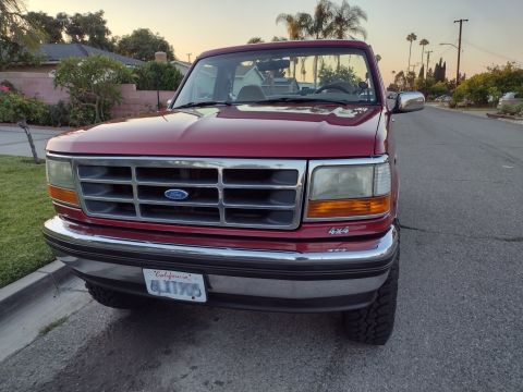 1994 Ford Bronco - Red Ford Bronco with a chrome grille and "4x4" badging is parked on a suburban street.