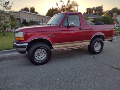 1994 Ford Bronco - This red Ford Bronco is parked on a residential street during sunset.