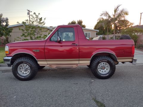 1994 Ford Bronco - This 1994 Ford Bronco is shown in a side profile, its distinctive red paint with tan accents and a spare tire mounted in the cargo area.