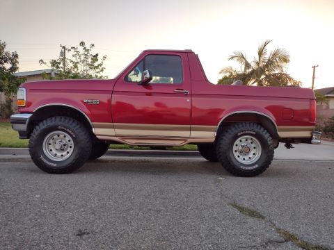 1994 Ford Bronco - Side view of a red 1994 Ford Bronco SUV with tan two-tone trim and large tires.