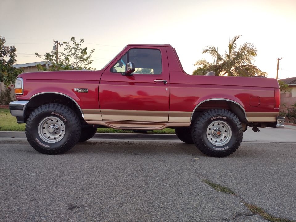 Red 1994 Ford Bronco with tan trim and aftermarket wheels, parked on a street