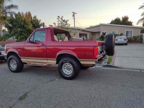 1994 Ford Bronco - A red 1994 Ford Bronco is parked on a residential street, showing its lifted suspension and off-road tires.