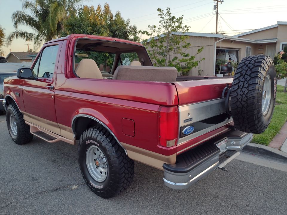 Red Ford Bronco with tan two-tone paint, spare tire on rear, viewed from the rear quarter