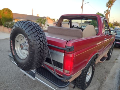 1994 Ford Bronco - Rear view of a red 1994 Ford Bronco, showing the spare tire and rear quarter panel.