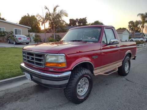 1994 Ford Bronco - A red 1994 Ford Bronco is parked in front of a house with palm trees and another car in the background.