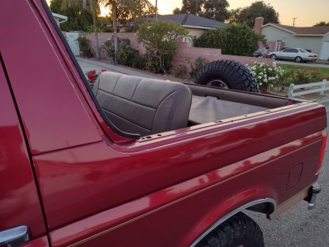 1994 Ford Bronco - Rear view of a red SUV with its top removed, revealing the interior seats and a spare tire mounted externally.