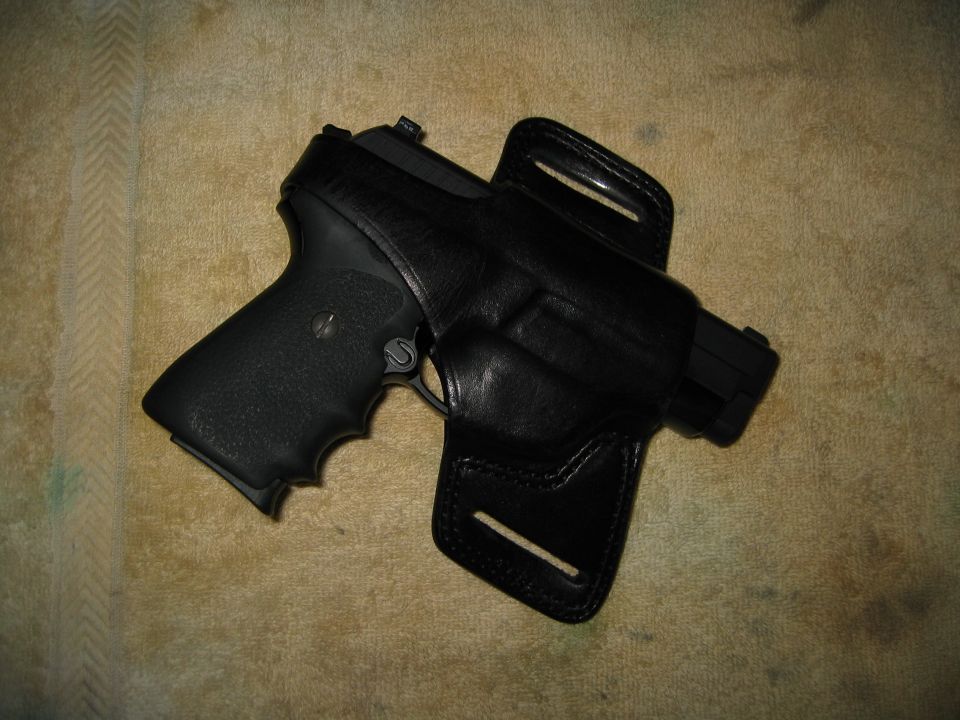 Black pistol in a black leather holster on a textured surface