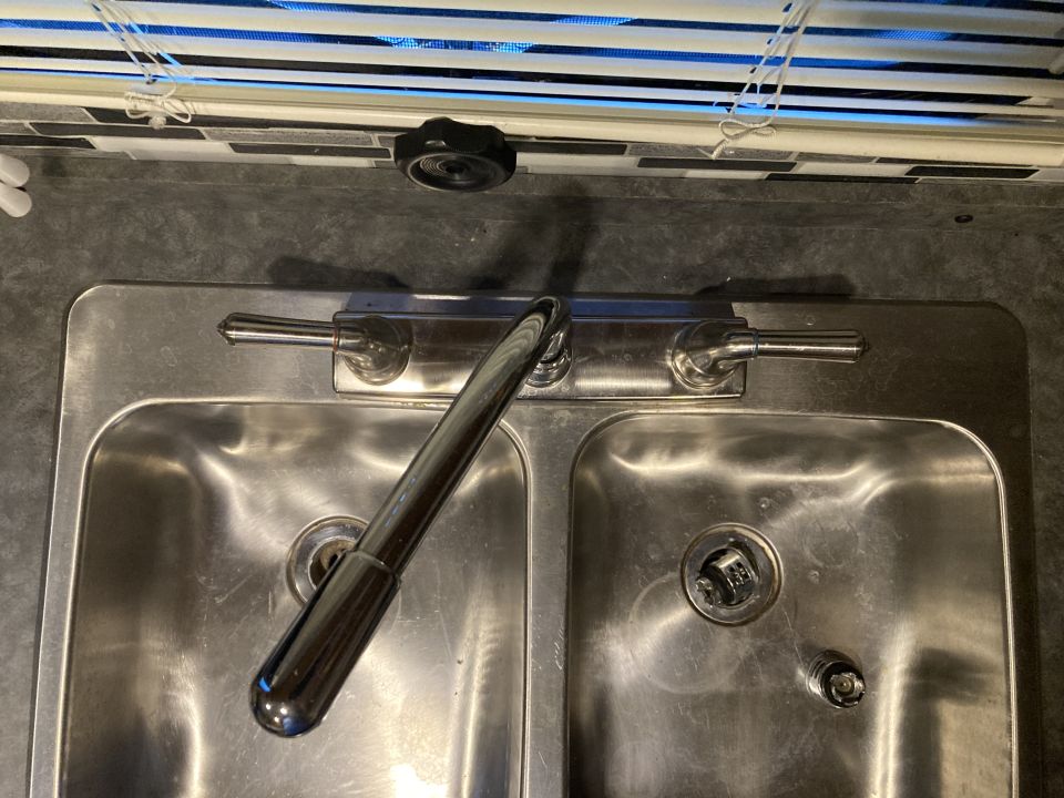 Double stainless steel sink with chrome faucet and handles. Blinds visible above