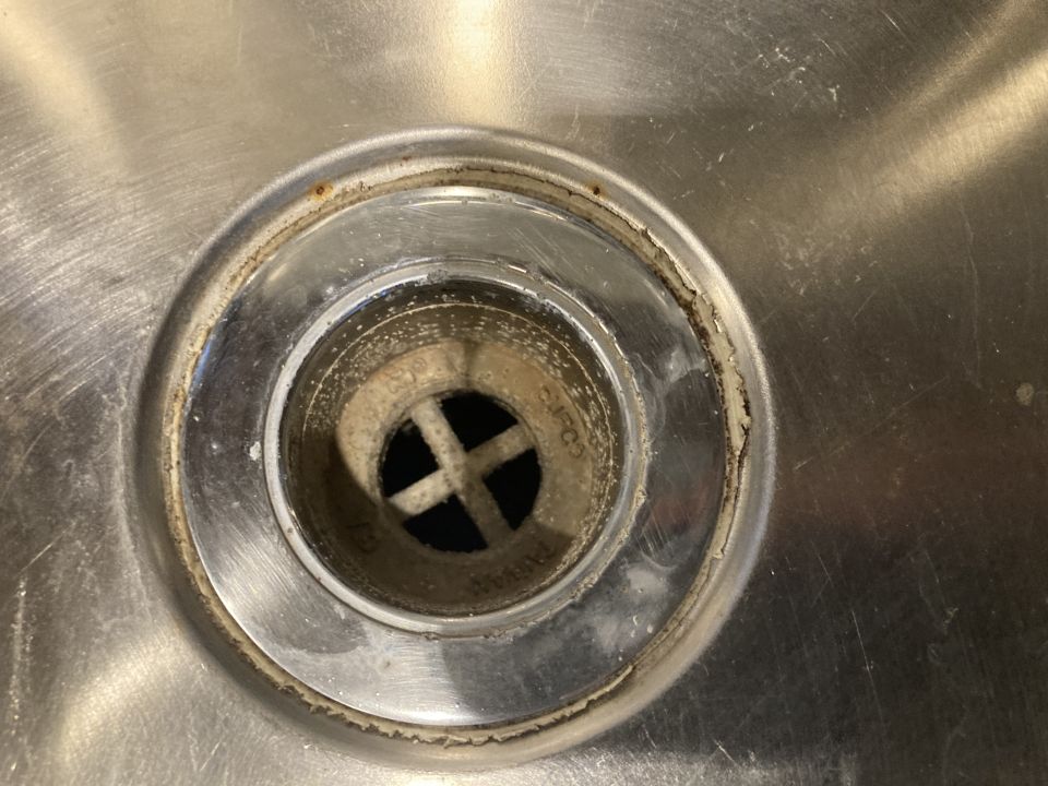 Close-up of a stainless steel sink drain with grime buildup around the rim