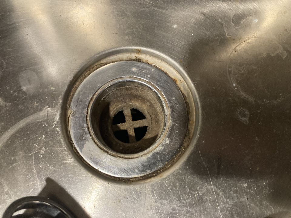 Close-up of a dirty sink drain with a cross-shaped strainer