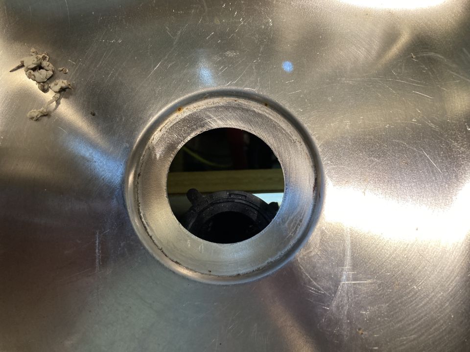 Close-up of a stainless steel sink drain opening with a black plastic fitting visible below