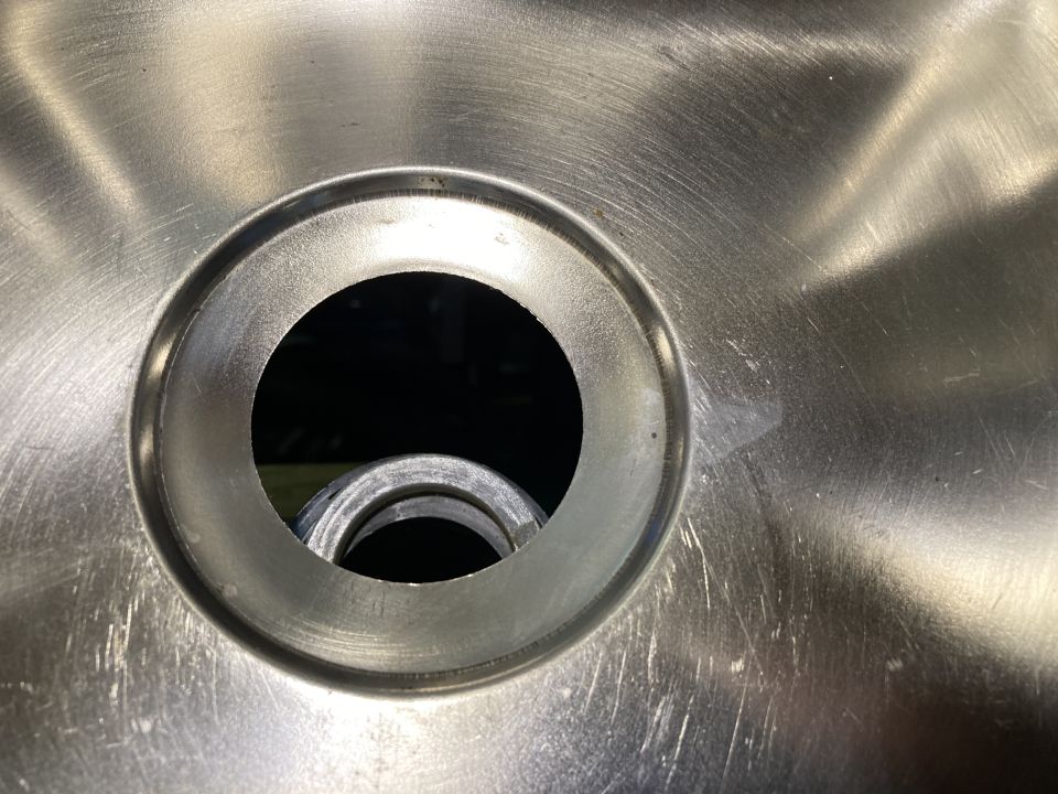 Close-up of a brushed metal surface with a circular opening and a pipe visible inside