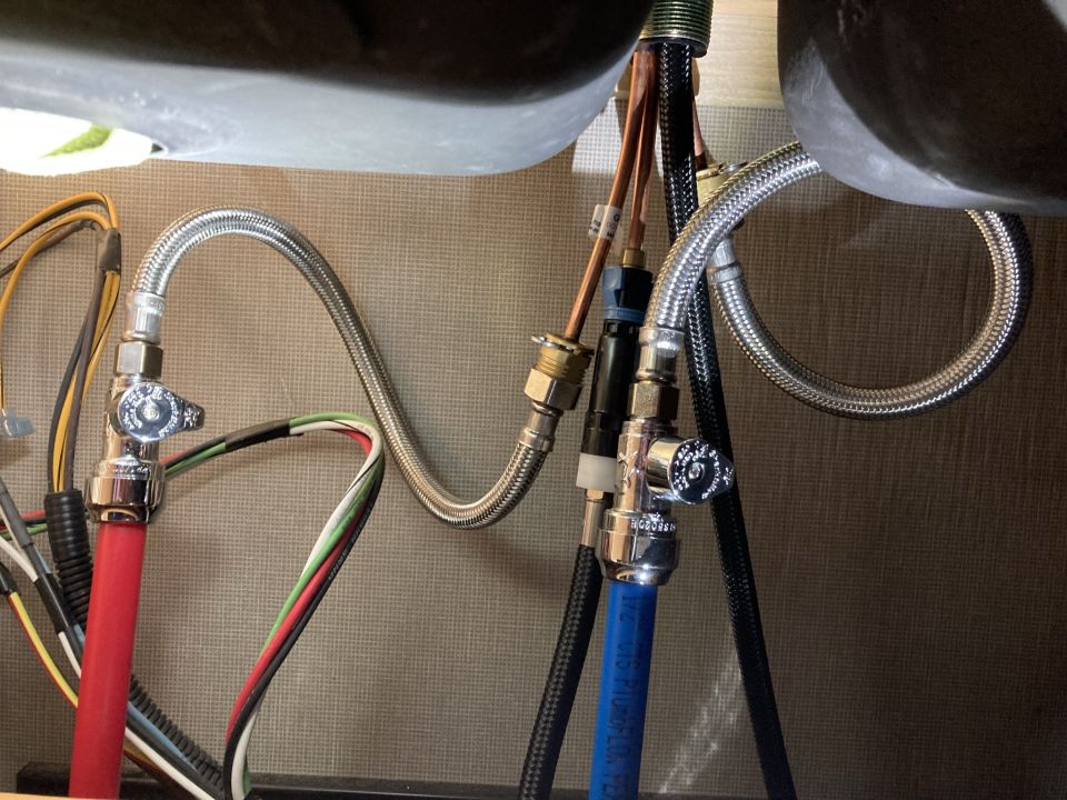 Plumbing lines and wires under a sink with chrome fixtures and braided hoses