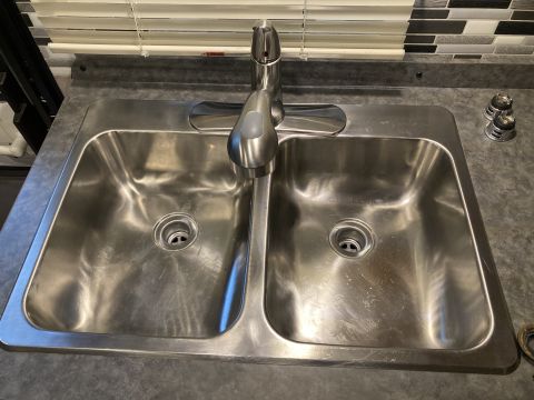 2015 Ford F-550 - A double stainless steel sink with a chrome faucet is shown, with a tiled backsplash and blinds in the background.