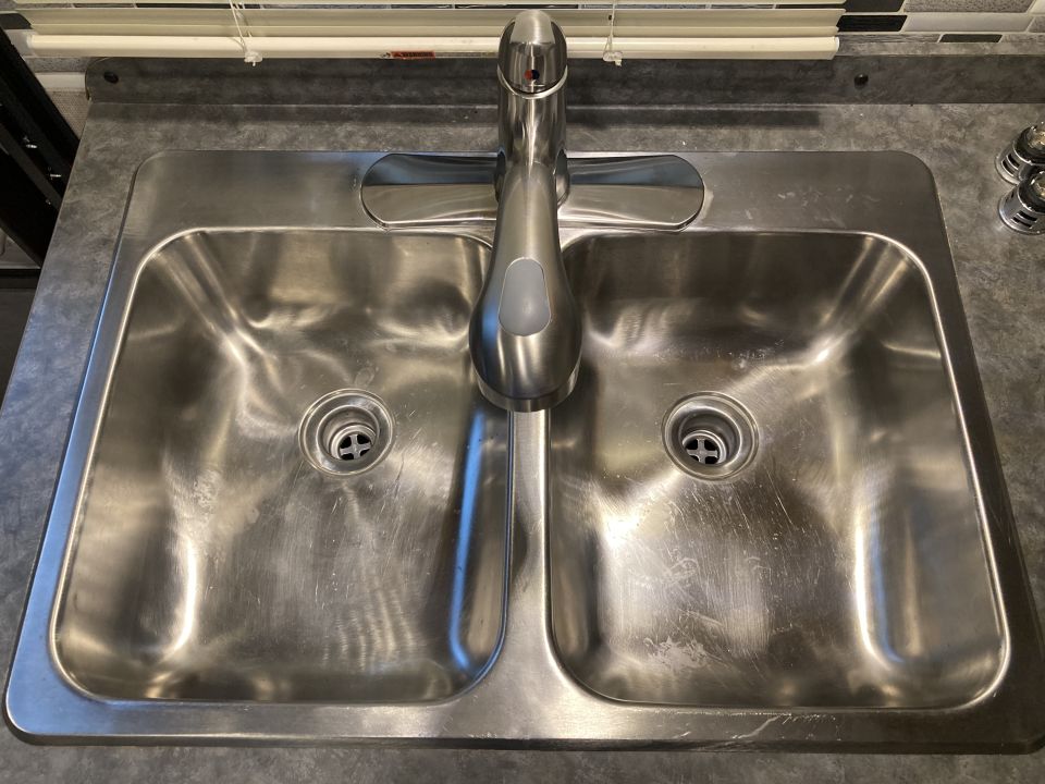 Stainless steel double sink with chrome faucet and drains. Some water spots visible