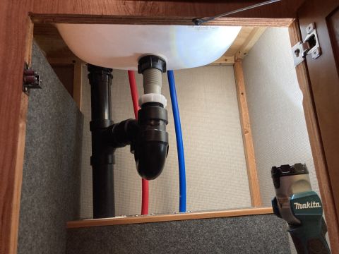 2015 Ford F-550 - Plumbing pipes and water lines are visible beneath a sink, with a Makita tool in the foreground.