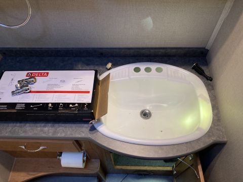 2015 Ford F-550 - A bathroom sink area with a new faucet box and a roll of toilet paper.