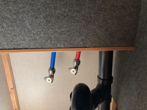 2015 Ford F-550 - Close-up of hot and cold water lines connected to shut-off valves, with a black drain pipe visible.
