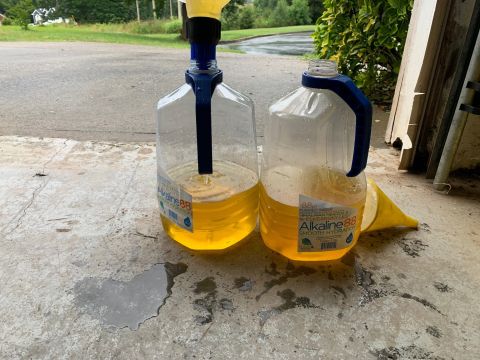 1996 Ford Bronco - Two large jugs of yellow liquid, likely oil or coolant, are being prepared for transfer using funnels.
