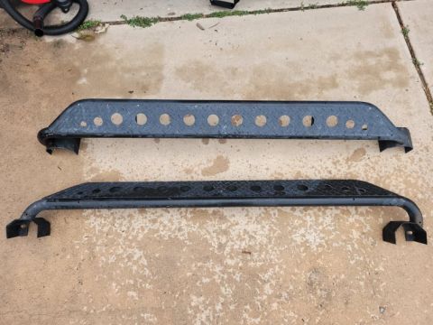 2015 Jeep Wrangler - A pair of aftermarket rock sliders are shown laid out on a concrete surface.